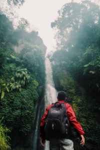 man wearing black backpack under waterfall